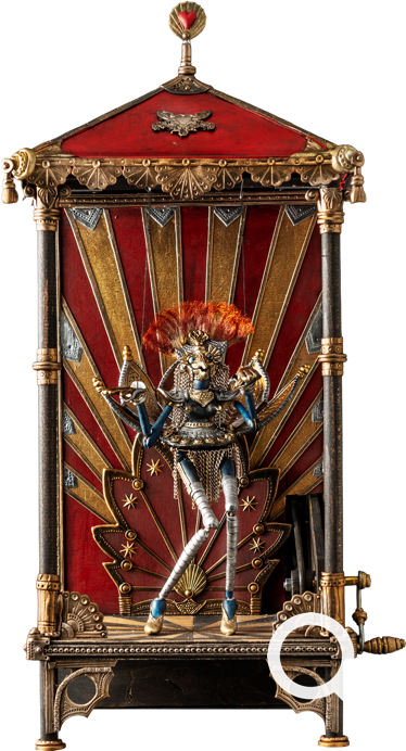 Metallfigur mit rotem Haar in einem dekorativen, rot-goldenen Geh&auml;use mit spitzem Dach.